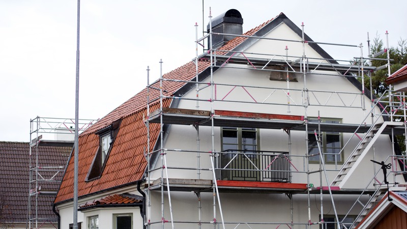 Byggnadsställningar är monterade vid ett enbostadshus för målning av fasad.