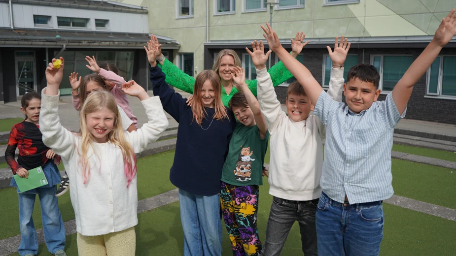 En grupp elever står ute på skolgården med händerna uppsträckta i luften.