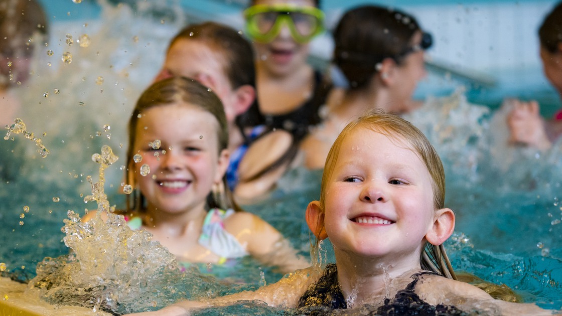 Fullt av badglada barn i bassängen på Kristianstads badrike