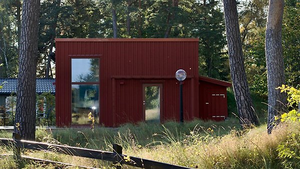 En mindre komplementbyggnad med röd träfasad i tallskogsmiljö.