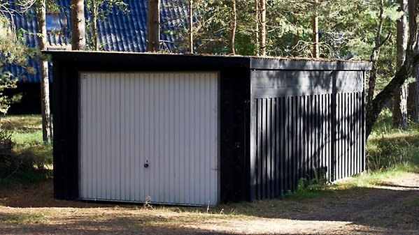 En liten och låg garagebyggnad i tallskogsmiljö.