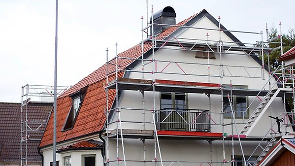 Byggnadsställningar är monterade vid ett enbostadshus för målning av fasad.