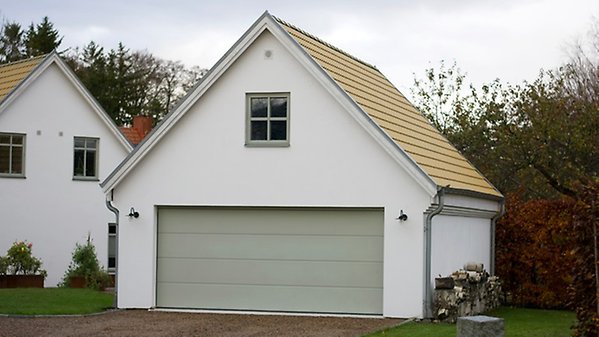 Garagebyggnad med vitputsad fasad, gult tak och ljusgrön garageport. Placerat i anslutning till ett bostadshus.