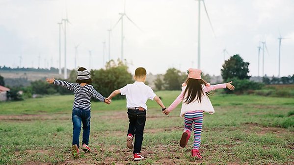 Happy children playing  outdoors. Kid having fun in green spring field against blue sky wind turbine background. Freedom and imagination concept